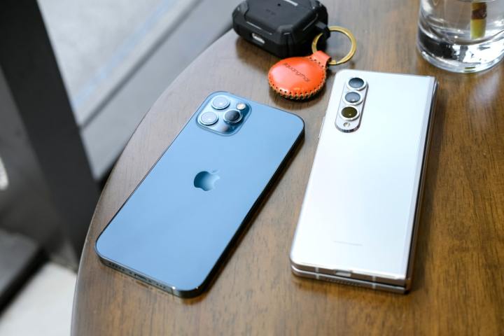 Un téléphone Samsung Galaxy et un iPhone côte à côte sur un bureau, à côté d'un Airtag Apple.