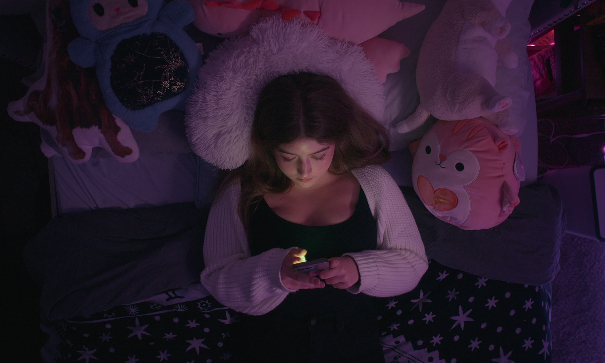 Une vue aérienne d'un jeune adolescent allongé sur son lit dans l'obscurité en regardant son téléphone d'une mauvaise influence: le côté obscur de Kidfluencing.