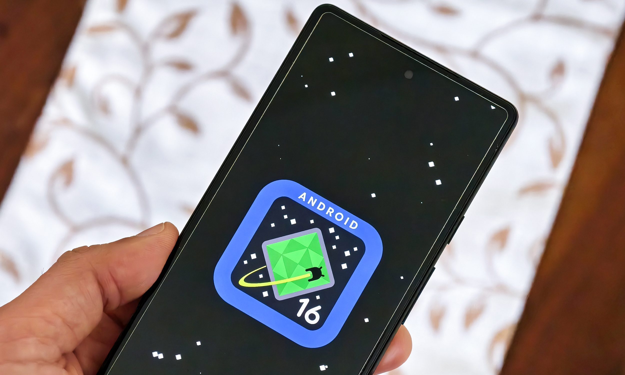 Logo Android 16 sur Google Pixel 6a tenu en main.