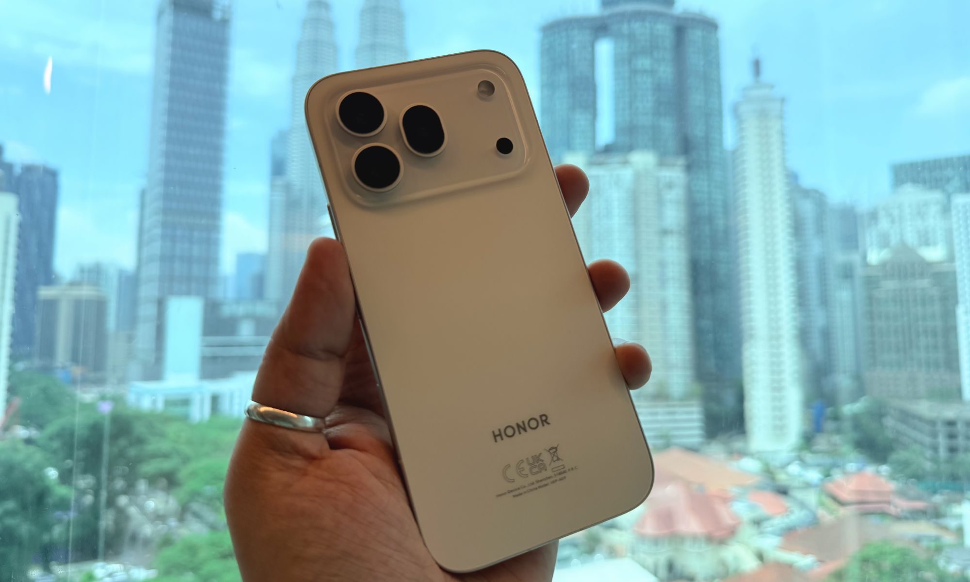Honor 600 Pro blanc à la main avec l'horizon de Kuala Lumpur en arrière-plan.