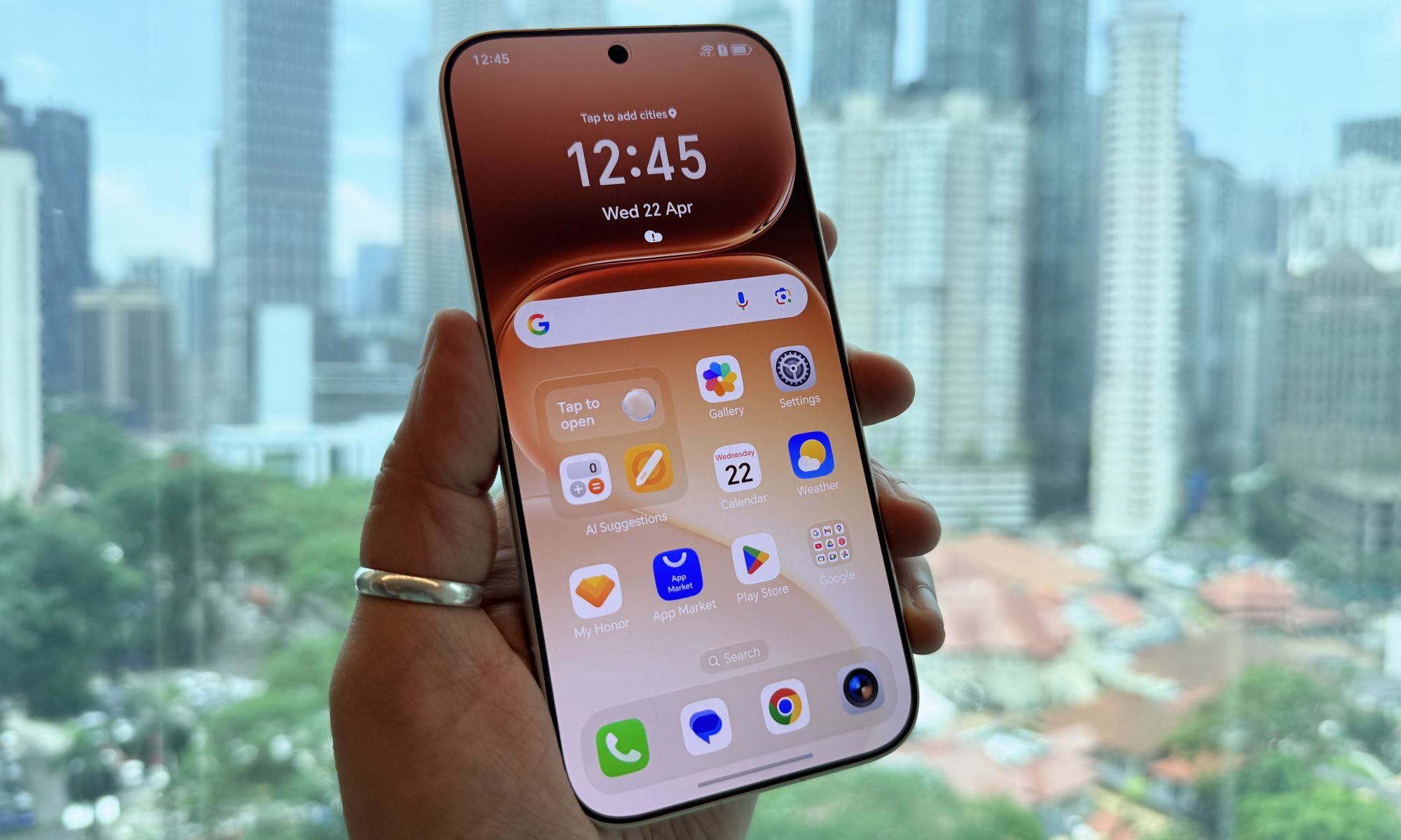 Honor 600 Pro en main montrant l'écran avec l'horizon de Kuala Lumpur en arrière-plan.