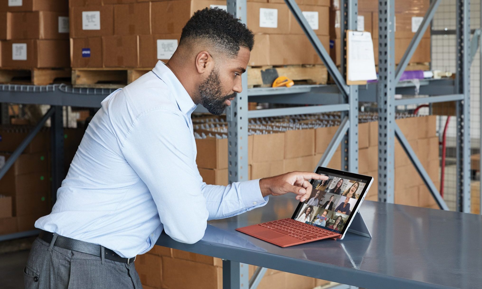 Un homme debout dans un entrepôt utilisant une tablette Surface pour passer un appel vidéo Teams