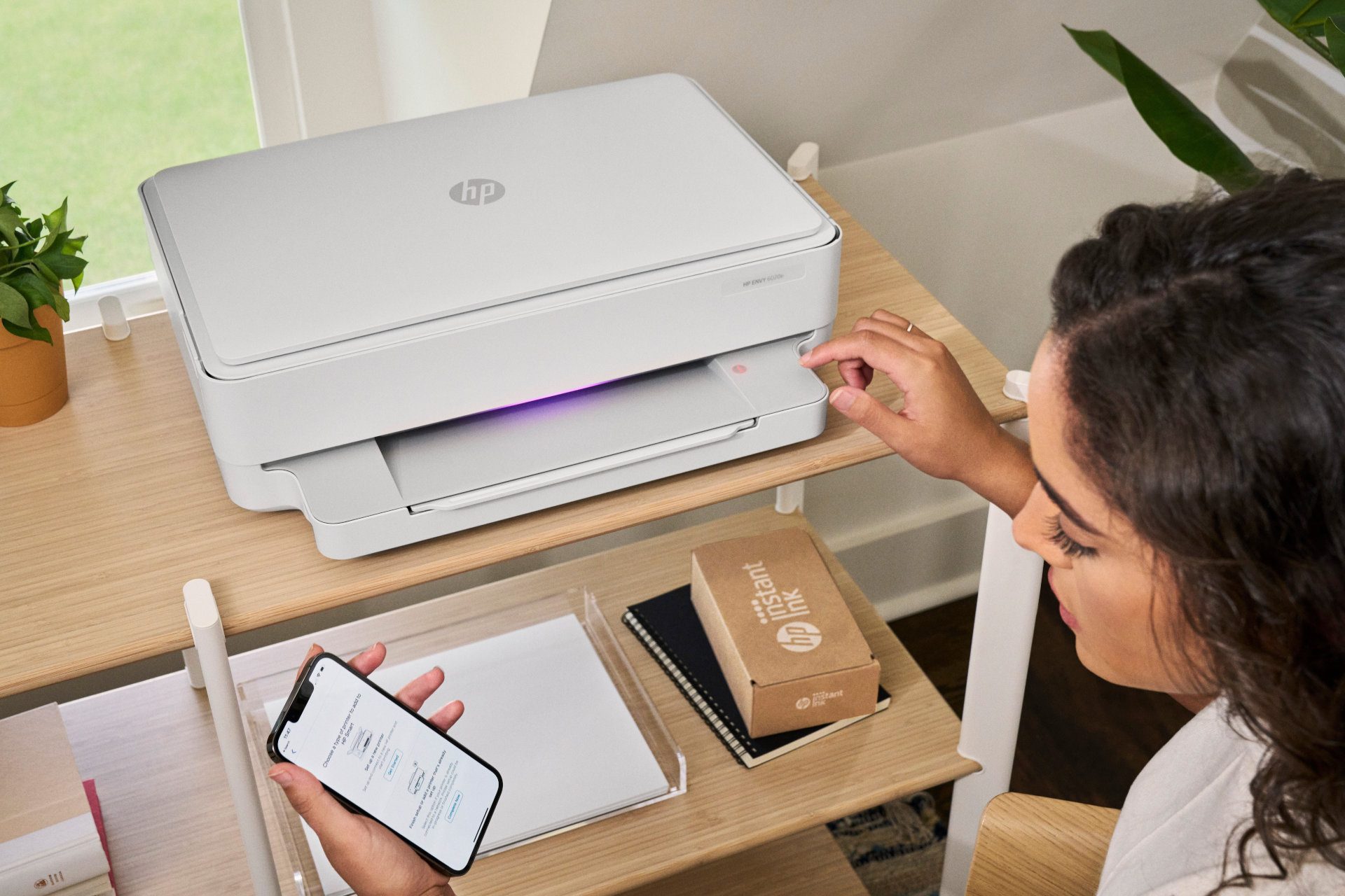 Une personne utilisant une imprimante HP Envy 6020e avec la boîte Instant Ink en vue.