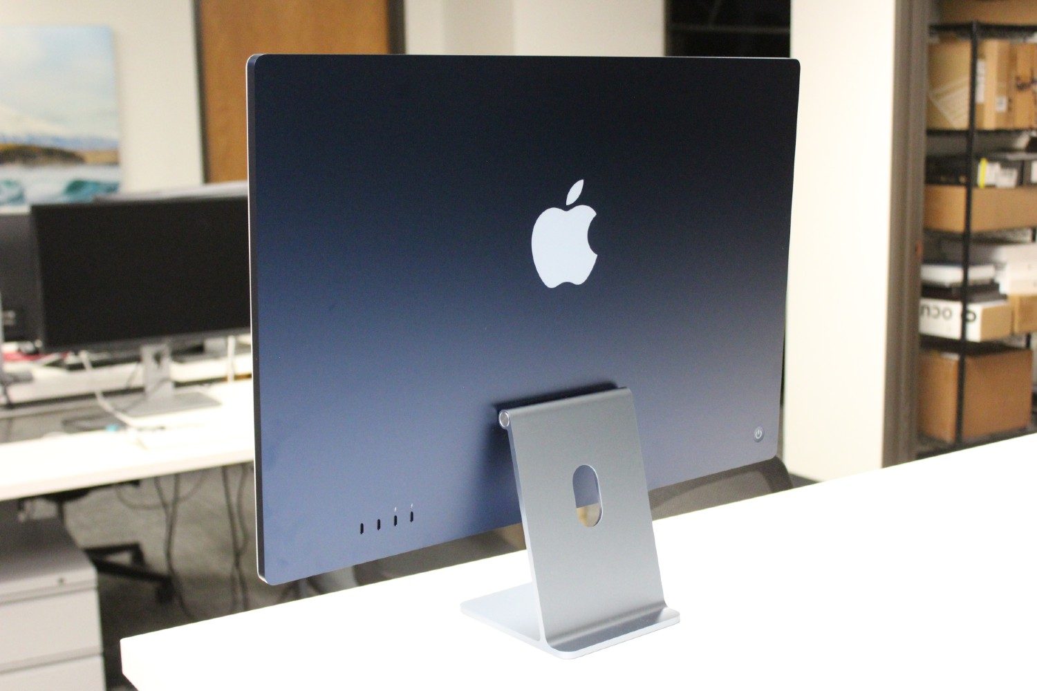 Le dos d’un iMac bleu sur un bureau blanc.