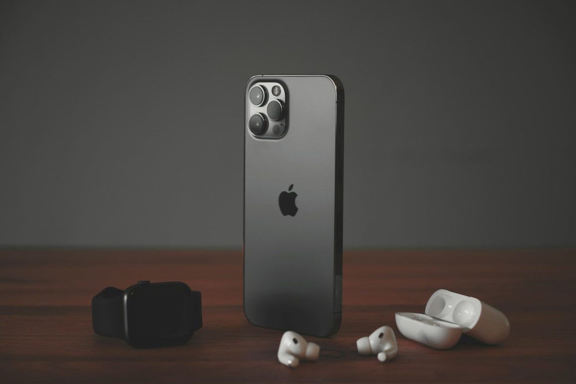 A smartphone, a smartwatch, and wireless earbuds on a wooden surface