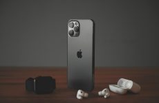 A smartphone, a smartwatch, and wireless earbuds on a wooden surface