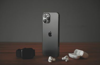 A smartphone, a smartwatch, and wireless earbuds on a wooden surface