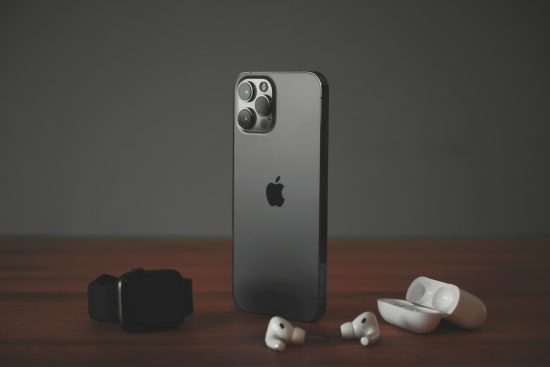 A smartphone, a smartwatch, and wireless earbuds on a wooden surface