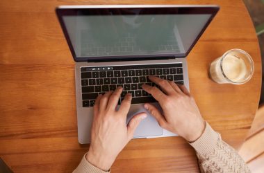 Mains sur le clavier d'un MacBook Pro posé sur une table en bois